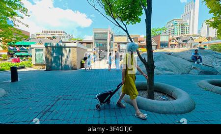 TORONTO, CANADA - 15 LUGLIO 2024: Una donna anziana trascina una borsa con le ruote attraverso la piazza pubblica lastricata di Yorkville Park a Toronto, Canada. Foto Stock