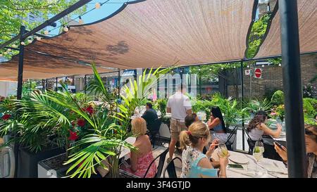 TORONTO, CANADA - 15 LUGLIO 2024: Gli ospiti godono di una cena all'aperto sotto una tenda parasole tra lussureggianti piante tropicali su una terrazza ristorante a Toronto, Can Foto Stock