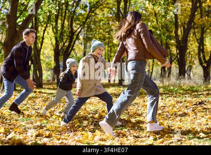 Famiglia che corre insieme nel parco autunnale, genitori e bambini che ridono tra le foglie Foto Stock