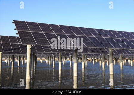 L'immagine mostra una vista parziale di una centrale solare galleggiante, con più file di pannelli solari neri sfalsati sostenuti da pilastri di cemento. Bene Foto Stock