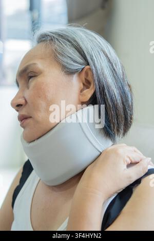 Paziente asiatica matura con collare cervicale o tutore per guarire una frattura dolorosa. Vista laterale, primo piano. Foto Stock