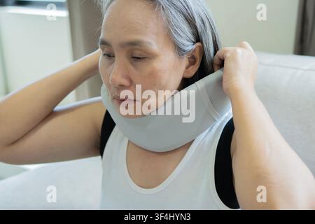 Donna asiatica matura che indossa un collare ortopedico e soffre di dolori al collo dopo un incidente. Concetto di dolore al collo. Concetto di Neckache. Foto Stock