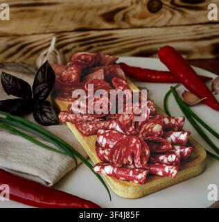 Salumi affettati assortiti e salsicce stagionate disposti su un tagliere di legno con erbe fresche e verdure. Antipasto tradizionale di salumeria. Foto Stock