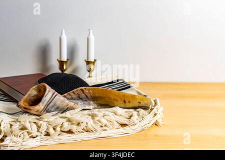 Simboli del nuovo anno ebraico tra cui shofar, tallit, kippah, libro e candele su un tavolo di legno Foto Stock