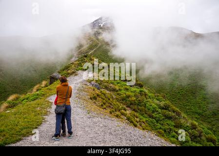 Escursionista con un bambino su un sentiero della cresta che osserva la cima nebbiosa del Monte Taranaki nel Parco Nazionale di Egmont, Nuova Zelanda, 5 gennaio 2024 Foto Stock