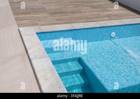 Vista ravvicinata di una piscina blu rinfrescante con scalini incorporati e un bordo realizzato con piastrelle effetto legno Foto Stock