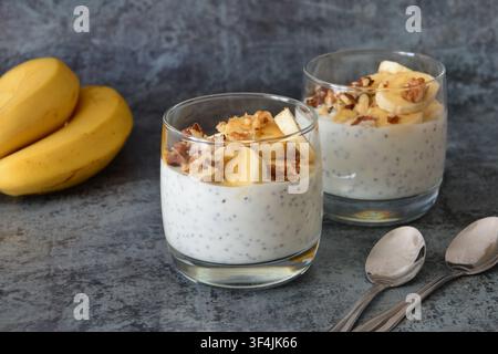 Pudding alla banana e ai semi di chia in bicchieri con cucchiai su sfondo scuro vista frontale Foto Stock