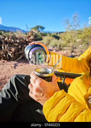 Primo piano di una donna che versa acqua calda da una thermos in una tazza da mate all'aperto nella natura Foto Stock