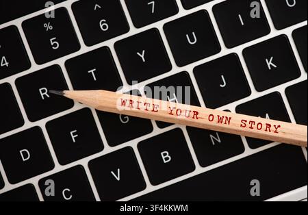Matita con il messaggio "Write Your Own Story" appoggiata su una tastiera di laptop, simboleggiante creatività, narrazione e sviluppo personale Foto Stock