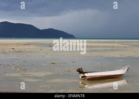Un piccolo bateau tradizionale per la pesca è arenato sulla sabbia con la bassa marea mentre una tempesta di monsoni si avvicina alla spiaggia di Thong Krut, Koh Samui, Thailandia. Foto Stock