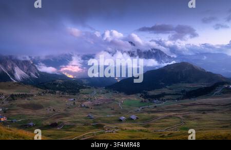 Vista sulla valle alpina con luci del villaggio e capanne di legno al crepuscolo Foto Stock