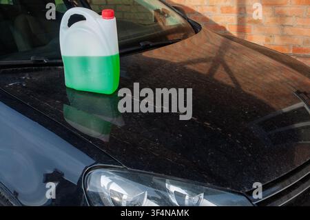 Liquido verde in un contenitore di plastica sul cofano nero polveroso di un'auto Foto Stock