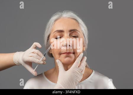 Anziana che riceve un'iniezione cosmetica in clinica, concetto di assistenza sanitaria Foto Stock