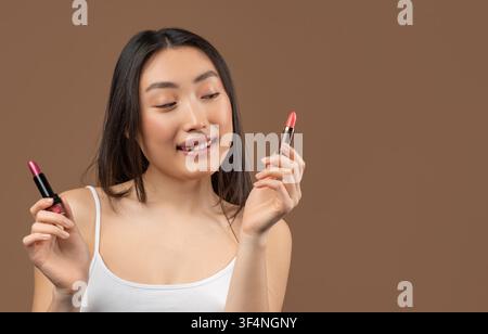 Giovane donna sorridente che tiene rossetti, concetto di prodotti di bellezza Foto Stock