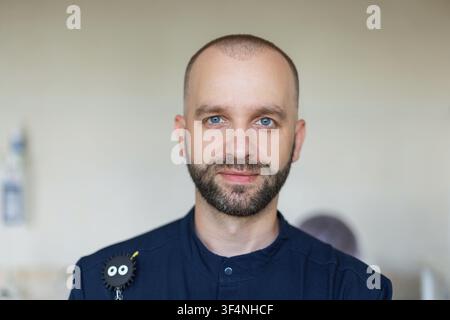 Ritratto ravvicinato di un medico o infermiere professionale maschile. Un uomo caucasico con occhi azzurri e barba, che indossa una divisa medica blu, che guarda la telecamera Foto Stock