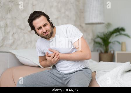 Uomo che sperimenta dolori al petto a letto, espressione preoccupata, concetto di assistenza sanitaria Foto Stock