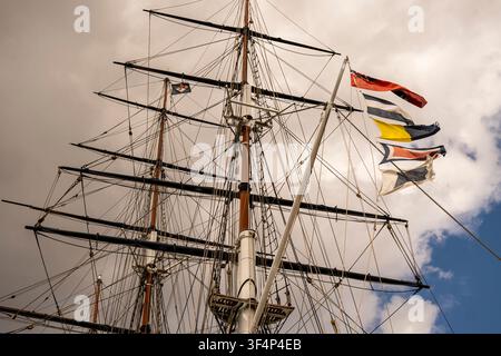 Alberi, attrezzatura complessa e bandiere segnaletiche colorate di una nave a vela storica contro un cielo nuvoloso. Foto Stock