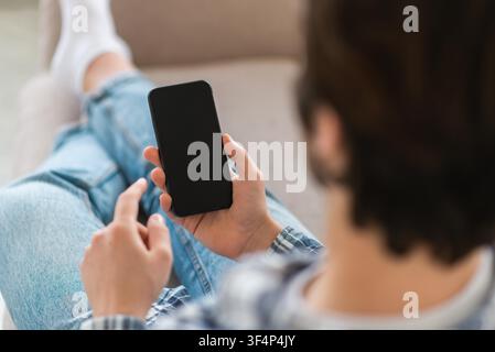Uomo irriconoscibile che usa uno smartphone seduto sul divano in salotto, concetto di relax Foto Stock
