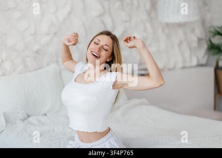 Giovane donna felice che si allunga a letto, mattina, nuovo inizio a casa Foto Stock