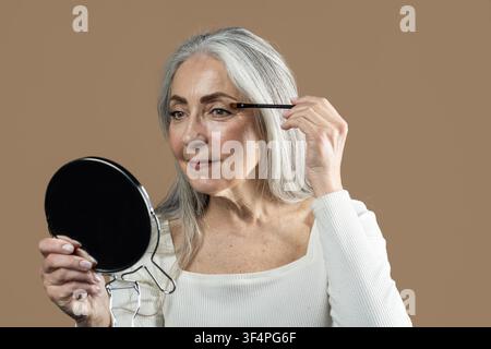 Anziana che si trucca davanti allo specchio, concetto di cura della pelle Foto Stock
