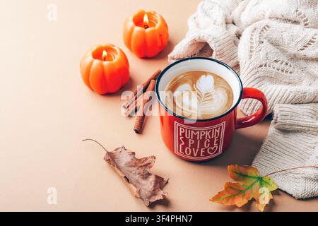 Latte autunnale con candele di zucca, bastoncini di cannella, coperta di maglia e foglie colorate che creano un'atmosfera stagionale calda. Foto Stock