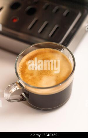 Prima piano di caffè nero appena preparato servito in una tazza di vetro trasparente con ricca crema, un concetto di bevanda calda e accogliente per caffetterie, colazione e ogni giorno Foto Stock