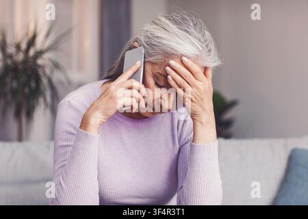 Donna anziana caucasica preoccupata che parla al telefono, ambiente domestico, concetto di assistenza sanitaria Foto Stock