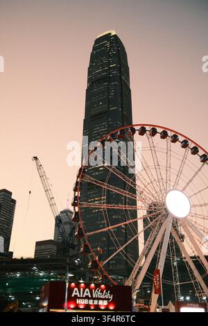 Il grattacielo del Two International Finance Centre si erge dietro alla ruota panoramica illuminata di Hong Kong alla Central Harbour Front, a Hong Kong. Foto Stock
