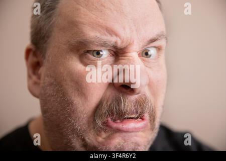 Primo piano di un uomo di mezza età con capelli grigi corti. Indossa una camicia scura e una leggera barba incolta. La sua fronte corrugata mostra frustrazione. Occhi spalancati e m Foto Stock