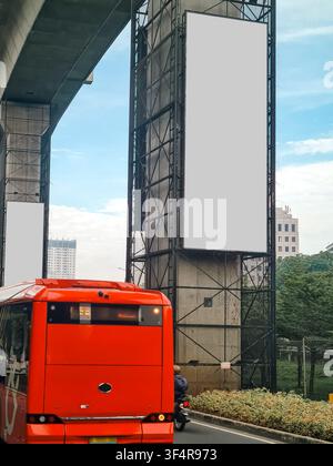 Ampio cartellone pubblicitario verticale vuoto su un pilastro dell'autostrada cittadina con un autobus pubblico rosso in primo piano. Ideale per mockup di media esterni Foto Stock