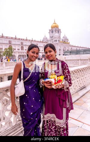 Due donne bengali sorridenti posano con una statua dorata del dio indù Gopal-Krishna da bambino davanti al Tempio d'Oro di Amritsar, in India. Foto Stock