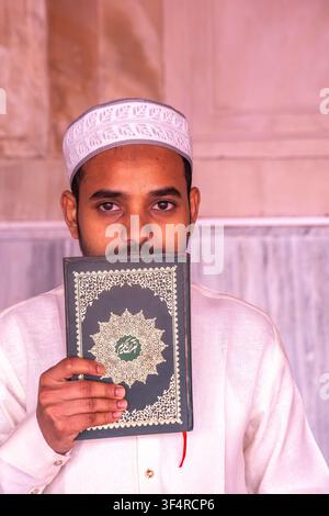 Un uomo che indossa una kufi e abiti tradizionali bacia il Corano in una moschea a Delhi, in India. Foto Stock