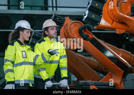 Discussione di squadra di ingegneri industriali sulla manutenzione del braccio robotico in un magazzino di fabbrica. Concetto di servizio di manutenzione di macchinari industriali pesanti, attrezzature Foto Stock