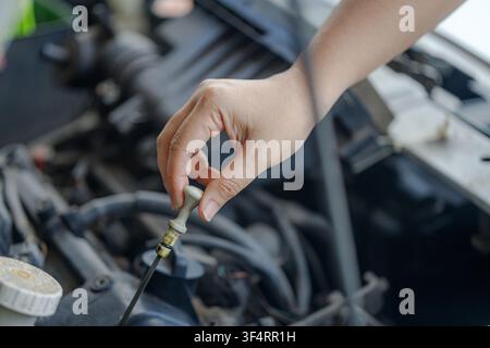 Primo piano di una mano di un meccanico che estrae la bacchetta del livello dell'olio motore per controllare il livello dell'olio, evidenziando la manutenzione del veicolo e la cura del motore in un ambiente di officina Foto Stock