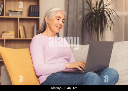 Donna caucasica anziana sorridente che usa un laptop a casa, concetto di stile di vita felice Foto Stock