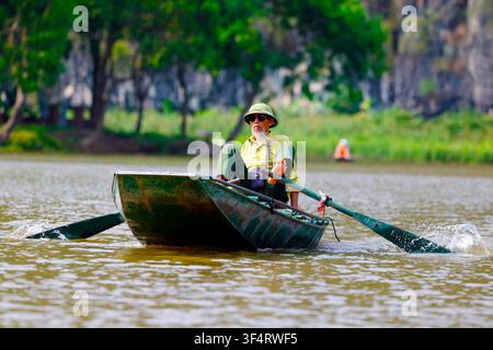 Un uomo di mezza età naviga lungo un fiume in una barca tradizionale nella regione di Hoa Lu. Tam Coc, Vietnam. Foto Stock