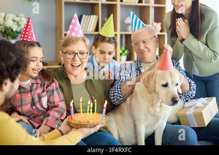 Felicità famiglia multigenerazionale compleanno a casa con torta, candele e Labrador Foto Stock