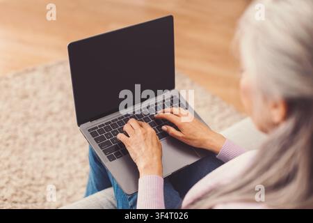 Donna anziana irriconoscibile che digita su un laptop, ambiente di ufficio domestico, concetto di lavoro da remoto Foto Stock