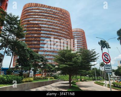Edifici per uffici ad alta altezza con rivestimento arancione unico e design cilindrico, sullo sfondo della vegetazione urbana e del cielo azzurro. Foto Stock
