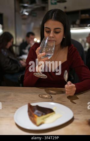 Giovane donna che mangia un dessert e beve acqua in un accogliente ristorante di notte Foto Stock