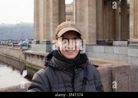 Giovane uomo sorride mentre si trova su un ponte in una città con architettura storica durante una giornata fresca. Ritratto dalla vita verso l'alto Foto Stock