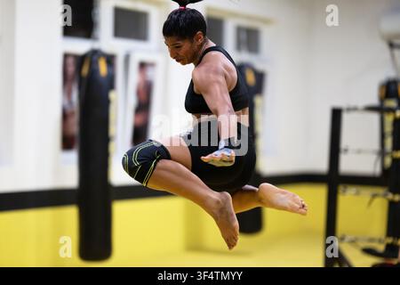 Atleta di arti marziali in salto a mezz'aria durante l'allenamento in palestra con ginocchiera e fasce per le mani Foto Stock