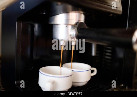 Portafiltro della macchina per l'espresso che estrae caffè ricco in due tazze bianche Foto Stock