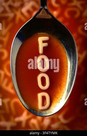 Prima verticale di un cucchiaio con zuppa di pomodoro e spaghetti alfabetici che formano la parola cibo su uno sfondo sfocato di zuppa Foto Stock