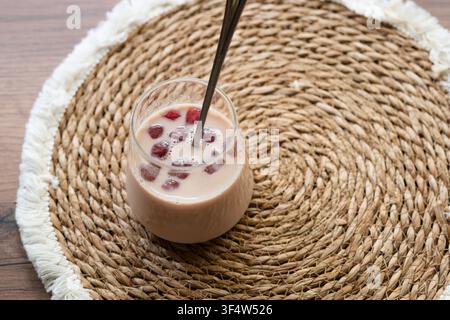 Caffè Bumble con succo di ciliegia ghiacciato in un bicchiere trasparente su un tavolo di legno. Bevanda estiva rinfrescante servita su un tessuto naturale Foto Stock