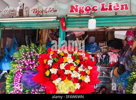 Mercato Han o Cho Han, negozio di fiori chiamato "Ngọc Liên", con un vivace mazzo di fiori rossi e gialli avvolto accanto ad arrangiamenti di orchidee viola. Foto Stock