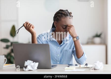 Stress di scadenza. Overworked femmina imprenditore nero massaggiando Nosebridge al posto di lavoro in ufficio Foto Stock
