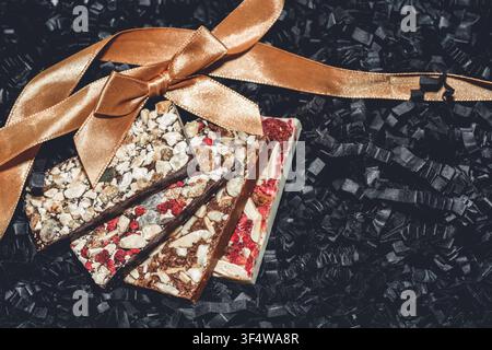 Barrette di cioccolato artigianali con un mix di noci, semi e frutta secca, adornate con un nastro dorato lucido e un fiocco Foto Stock