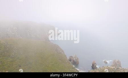 Vista aerea della costa frastagliata di Cabo da Roca in Portogallo, dove scogliere rocciose incontrano l'oceano Atlantico attraverso una fitta nebbia costiera Foto Stock