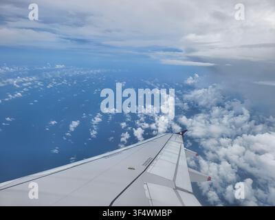 Vista ad alta quota di soffici nuvole bianche sotto un cielo blu terso, come visto dal finestrino di un aereo passeggeri. Foto Stock